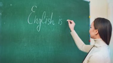 Genç pedagog eğitim merkezinde tebeşirle tahtaya yazı yazıyor. Çekici öğretmen sınıftaki bir tahtaya İngilizce kelimeler yazıyor..