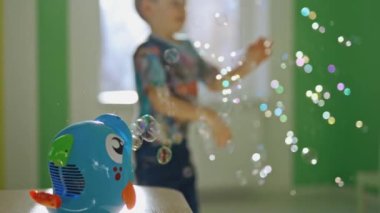 Balık şeklinde baloncuk üfleyici ve sabun köpüğüyle oynayan küçük bir çocuk. Meraklı küçük çocuk evdeki odada sabun köpüğü patlatıyor..
