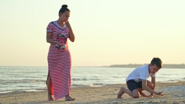 海岸上的一个女人和一个男孩暑假期间 穿着长裙的母亲和儿子一起在沙滩上玩得很开心 — 图库视频影像