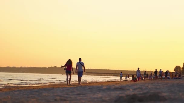 日没のビーチに沿って歩く男と女のバックビュー 人々は夕方に海辺から家に帰る — ストック動画