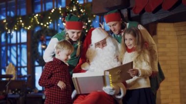 Albümlü çocuklar, elfler ve Noel Baba. Noel Baba fotoğraf albümü tutuyor. Elfler ve çocuklar Noel Baba 'yla dekore edilmiş odada çok eğleniyorlar. Mutlu Noeller..