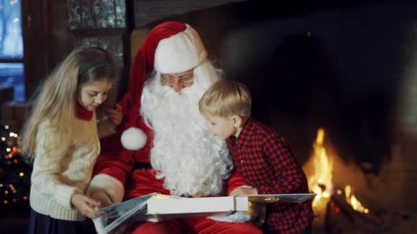 Dzieci Patrzą Album Ręce Mikołaja Przy Kominku Święty Mikołaj Białą — Wideo stockowe