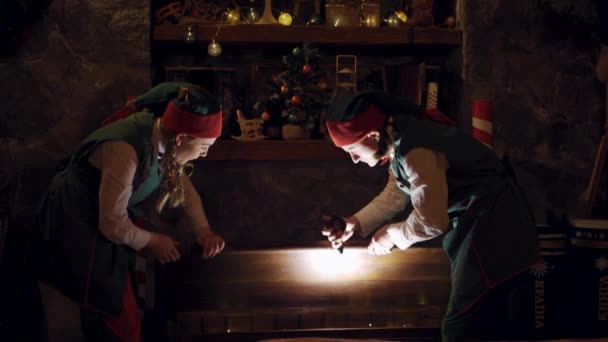 クリスマスの暗い部屋の妖精のエルフ 興奮したエルフの魔法の胸を開き 屋内で贈り物を取り出します クリスマスタイム — ストック動画