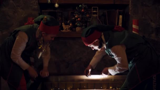 驚いたエルフは暗闇の中で大きな胸を開ける サンタのヘルパーは魔法の胸を開き クリスマスの装飾の背景に美しい箱を取る — ストック動画