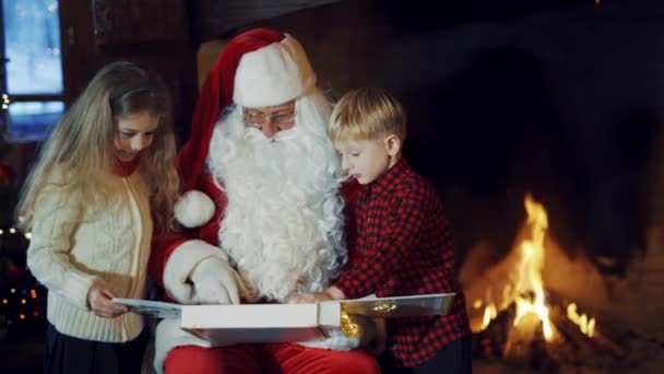 Chłopiec Dziewczynka Patrzą Album Rękach Mikołaja Tle Kominka Święty Mikołaj — Wideo stockowe