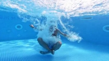 Adam yoga pozisyonunda havuzun berrak sularına atlıyor. Sualtı kamerası suya atlayan bir adamın videosunu çekiyor. Erkek, el hareketini su altında yapar..