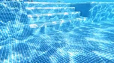 Yüzme havuzunda su altında şeffaf bir arka plan. Bir çocuğun cesedi su altında merdivenlerden aşağı inerken ve mavi berrak suda yüzerken görülüyor..