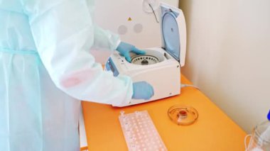 Kadın bilim adamı, laboratuardaki bir santrifüje birkaç şişe sıvı yüklüyor.. 