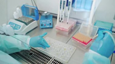 Mavi steril eldivenli eller test tüplerini sıvıyla dolduruyor. Modern laboratuvarda, içinde sıvı bulunan raflar..