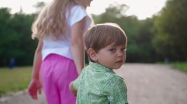 Üzgün çocuk küçük bir kızla eve gidiyor. İki çocuğun el ele tutuşması ve yazın parkta yürümesi..