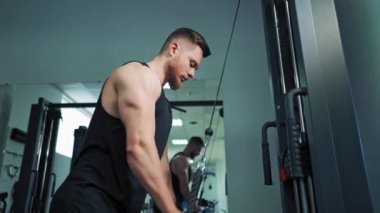 Kaslı adam fitness merkezinde simülatörde çalışıyor. Güçlü bir sporcu halatla çubuğu çeker ve ağırlık kapalı alanda çalışır..