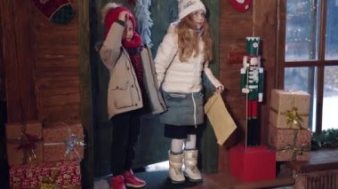 Zarflı küçük bir çocuk ve kız Noel Baba 'ların evine geliyor. Çocuklar Noel 'de dekore edilmiş evin içine harika bir şekilde bakıyor..
