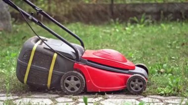 Bahçede çim biçme teknolojisi. Kırmızı çim biçme makinesi arka bahçede çim biçiyor. Dışarıdaki elektrikli çim makinesi..