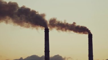 Büyük endüstriyel borular atmosferi dumanla kirletir. Gri gökyüzü arka planında havada kalın dumanlı iki büyük boru..