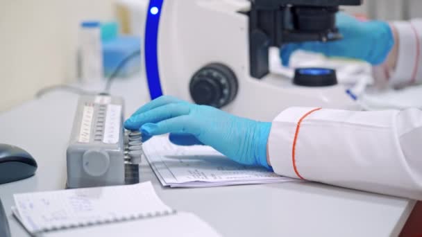 戴着医生蓝色手套的手 实验室科学家在桌上用显微镜工作 后续行动 — 图库视频影像