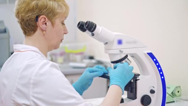 医疗中心有显微镜的实验室助理 女科学家正在通过显微镜用样品进行研究 — 图库视频影像