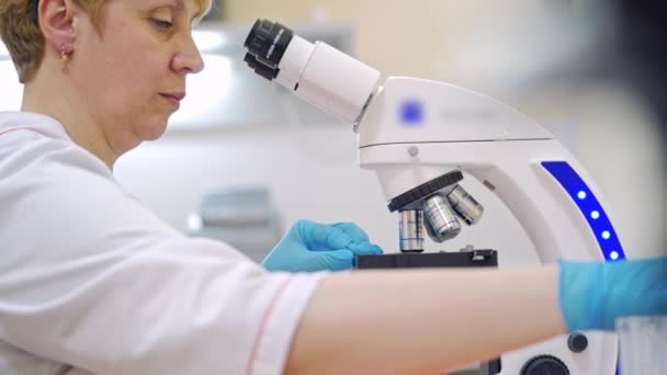 現代の顕微鏡で働く女性科学者 女性科学者は研究室で顕微鏡を通して生物学的サンプルを研究します — ストック動画