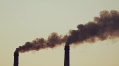 Kalın dumanlı iki boru havayı dolduruyor. Arka plandaki fabrika borularından gelen kara dumanlar. Çevre kirliliği.