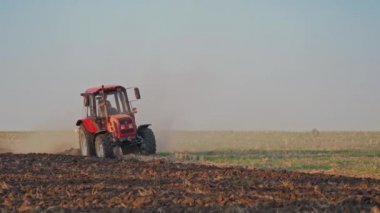 Kırmızı traktör iş başında. Tarım makinesi gündüz tarlayı sürüyor. Açık havada arazi ekimi.