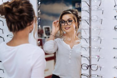 Gözlüklü kadın. Gözlük seçiyorum. Optikteki müşteri. Seçici odaklanma. Gözlüklü kadın kameraya bakıyor. Gözlükleri takın. Dükkanda geniş çeşitlilik.