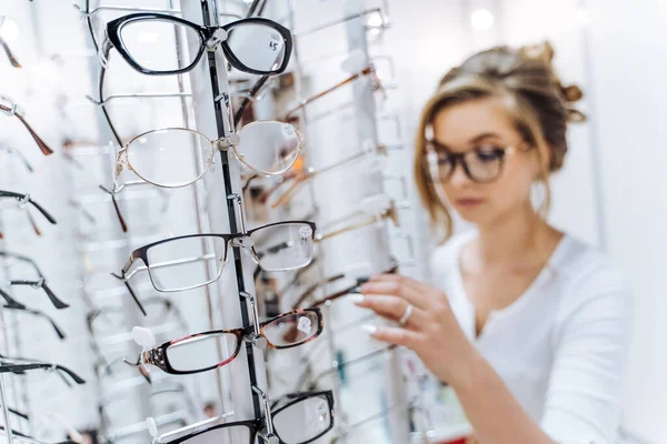 店内にはファッションエレガンスの眼鏡のスタンド 現代の眼科店でメガネ付きのショーケース 背景に女性 — ストック写真