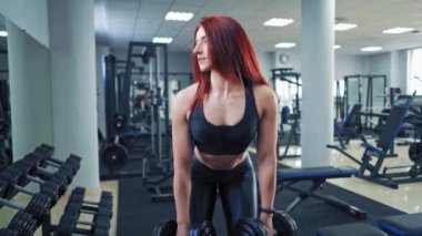 Spor salonundaki antrenman sırasında kızıl saçlı sporcu kadın. Siyah bluzlu çekici bir bayan sporcu ve aynanın yanında dambıl kaldırıyor..