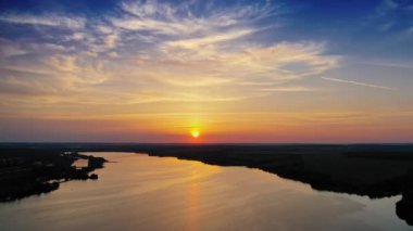 Akşam gölünün sakin suları. Gün batımında nehir üzerindeki doğal orman ve tarlaların arasındaki hava manzarası. Kamera geri gider.