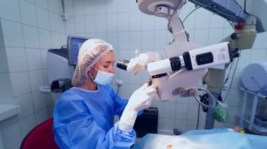 Uzman, ameliyathanedeki hastanın gözlerindeki mikroskoptan bakıyor. Kadın cerrah, modern ekipmanlarla özel klinikte çalışıyor..