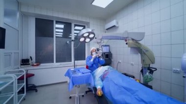 Hasta klinikte yatıyor ve doktor mikroskopla gözleri inceliyor. Oftalmolog, kapalı alandaki modern ekipmanlarla hastanın gözlerine bakıyor..
