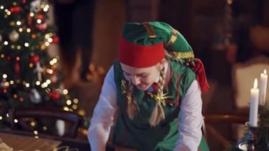 Noel süslemeli odada mutlu bir elfin portresi. Yeşil kostümlü, kırmızı ve yeşil şapkalı komik kadın bir zarf seçiyor..