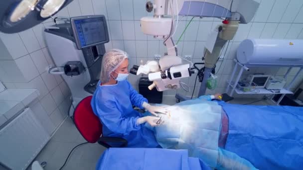 女外科医生戴着手套和面罩 用显微镜对眼睛进行手术 眼科医生在现代诊所治疗病人的眼睛 — 图库视频影像
