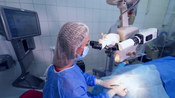 専門医が目で手術を行います 保護制服の女性医師は 私立クリニックで目の手術中に近代的な顕微鏡を使用しています トップ表示 — ストック動画