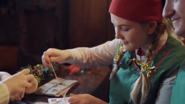 クリスマスにはエルフと子供が封筒を作っている テーブルの上に多くのクリスマスの手紙とかわいい子供は封筒にシールを置きます — ストック動画