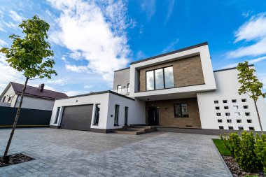 Garajı olan modern lüks bir ev. Yukarıdaki mavi gökyüzü. Bahçede kimse yok. Modern mimari.