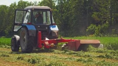 Modern traktör kırsalda yeşil çimenleri kesiyor. Bir yaz günü tarlada hayvanlara çim biçmek için kullanılan bir tarım makinesinin arka plan görüntüsü.