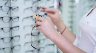 Dükkanda yeni gözlük deneyen genç bir kadının yan görüntüsü. Optik mağazasında şık gözlük tutan güzel bir müşteri..