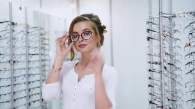 Optik mağazasında gözlüklü güzel bir modelin portresi. Modern gözlük dükkanında yeni gözlük takan genç bir kadın kameraya poz veriyor..