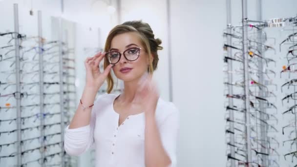 一个在光学商店配眼镜的漂亮模型的肖像 在现代眼镜商店里 年轻女子穿着新的时髦眼镜 摆出一副拍照的姿势 — 图库视频影像