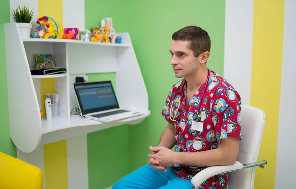 Pediatrician in bright medical scrubs. Doctor physician in cabinet. Man sitting at chair giving consultation.