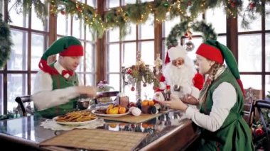 Elfler ve Noel Baba Noel 'de masada. Neşeli peri karakterleri yeni yılda tatlı ve kurabiye yerken birlikte harika vakit geçiriyorlar..