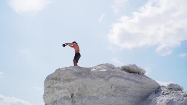 一个壮汉在白山提起水壶的侧视图 男子运动员用双手在室外美丽的自然背景上挥动水壶铃铛 — 图库视频影像