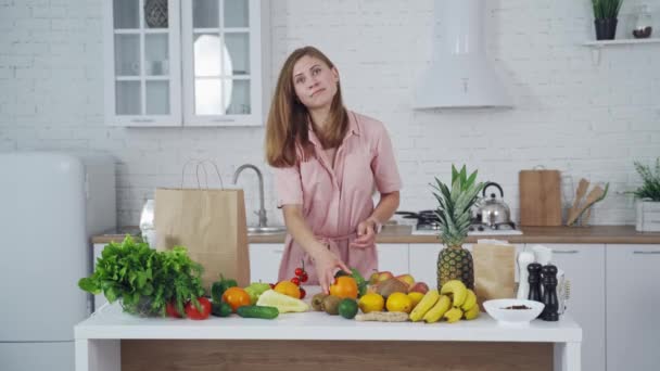 快乐的女人在厨房里从纸袋里拿出新鲜的水果 桌上有有机水果和蔬菜 室内有漂亮的女性 健康的生活方式 — 图库视频影像