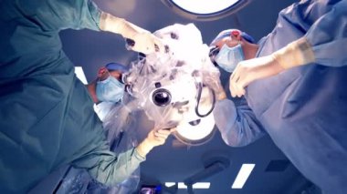 Aşağıdan bir mikroskop ve iki uzman içeriyi inceliyor. Nörocerrahlar klinikte ameliyat sırasında modern mikrofon kullanıyorlar..