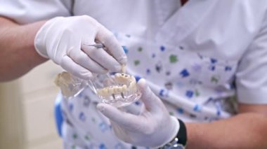 Doktor plastik çene örneğinde ya da diş tedavisinde farklı yöntemler gösteriyor. Modern diş sağlığı kliniği geçmişi. Sağlık konsepti. Erkek doktorun ellerinde beyaz tıbbi eldivenler..