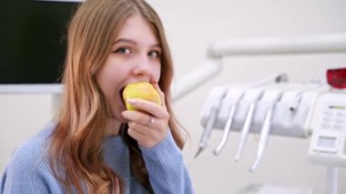 Genç bir kadın modern diş kliniğinde elma yiyor. Sağlıklı diş kavramı. Hassas diş sorunu çözülüyor..