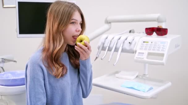 若い女性は現代の歯科医院でリンゴを食べる 健康な歯の概念 敏感な歯の問題を解決する — ストック動画