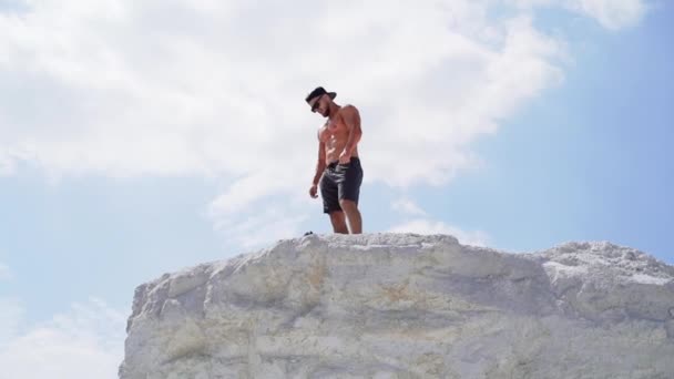 在山上戴着帽子和眼镜的无袖运动员 从下面看一个站在白山顶上的运动员 — 图库视频影像