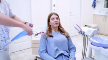 Diş konsepti. Genç bir kadın dişçi ofisine geliyor ve sandalyeye oturuyor. Erkek stomatolog hastanın dişlerini tedavi etmeye başlar..