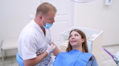 Dişçi kadın bir hastayla konuşur. Profesyonel doktor kadın hastaya dişlerine nasıl bakacağını açıklıyor. Güzel bir kadın klinikte stomatologu ziyaret ediyor..