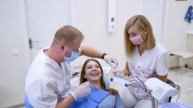 Hasta ile çalışan dişçi asistanı. Profesyonel stomatolog, gülümseyen kadın için yapay diş rengini seçiyor. Diş implantlarının faydaları.